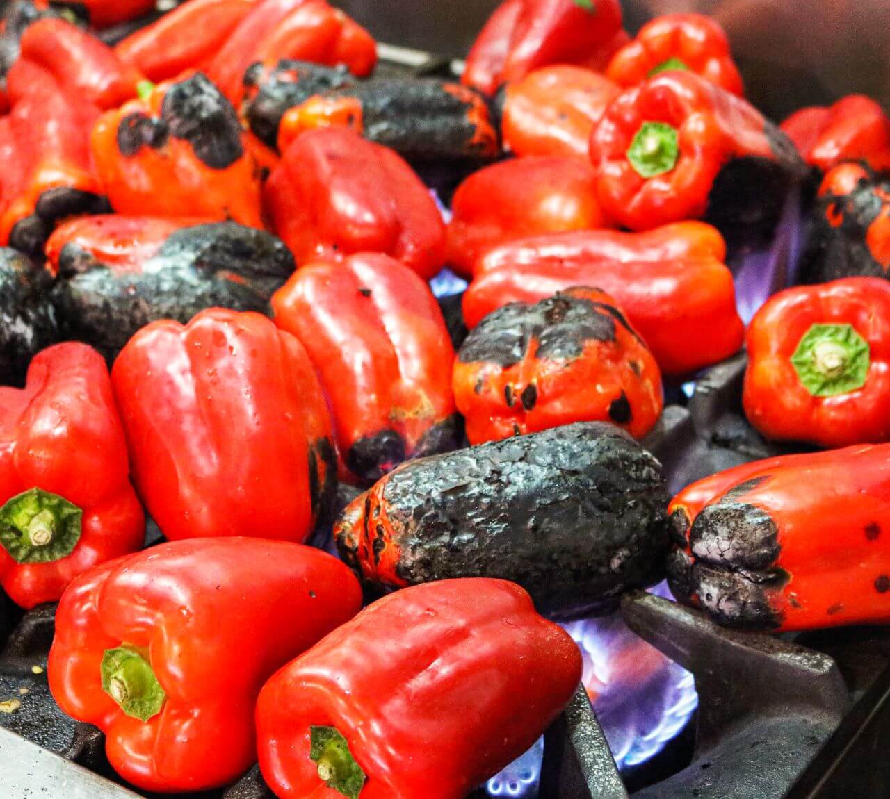 A bunch of red capsicums being burned on the stove